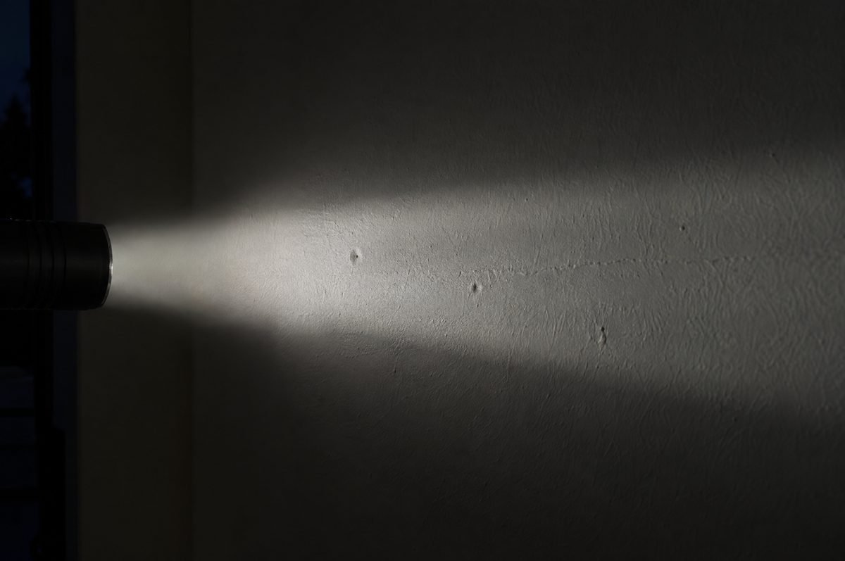 A torch beam raking across a plain wall at night, showing small dents and a faint ridge in the surface.